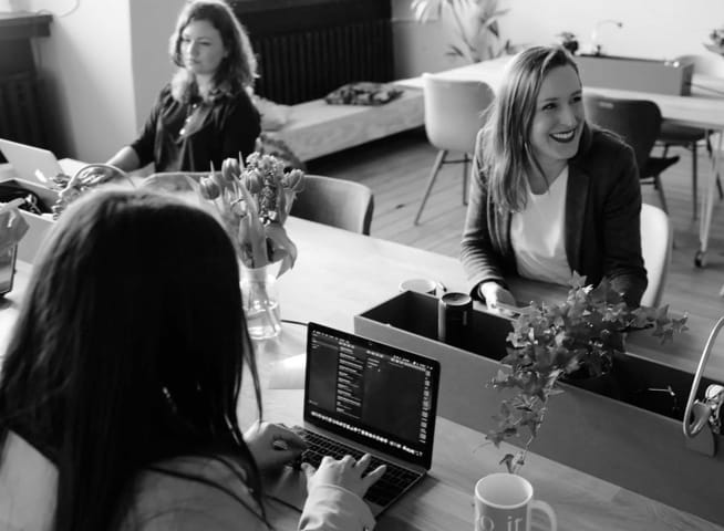 three woman working on a large table in front of laptops.